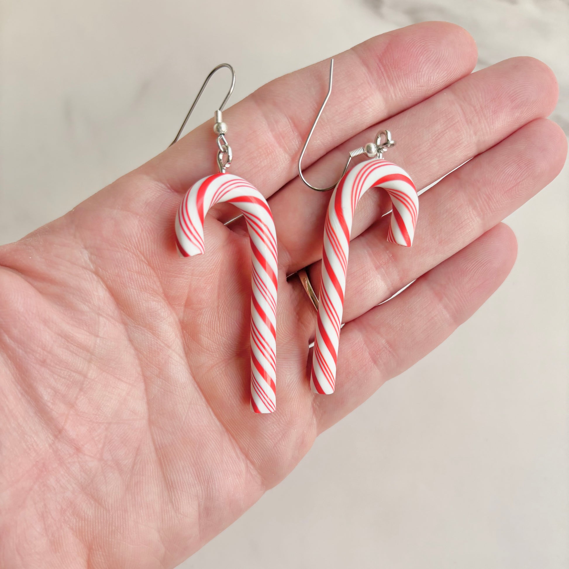 Candy cane-shaped earrings held in a hand against a neutral background