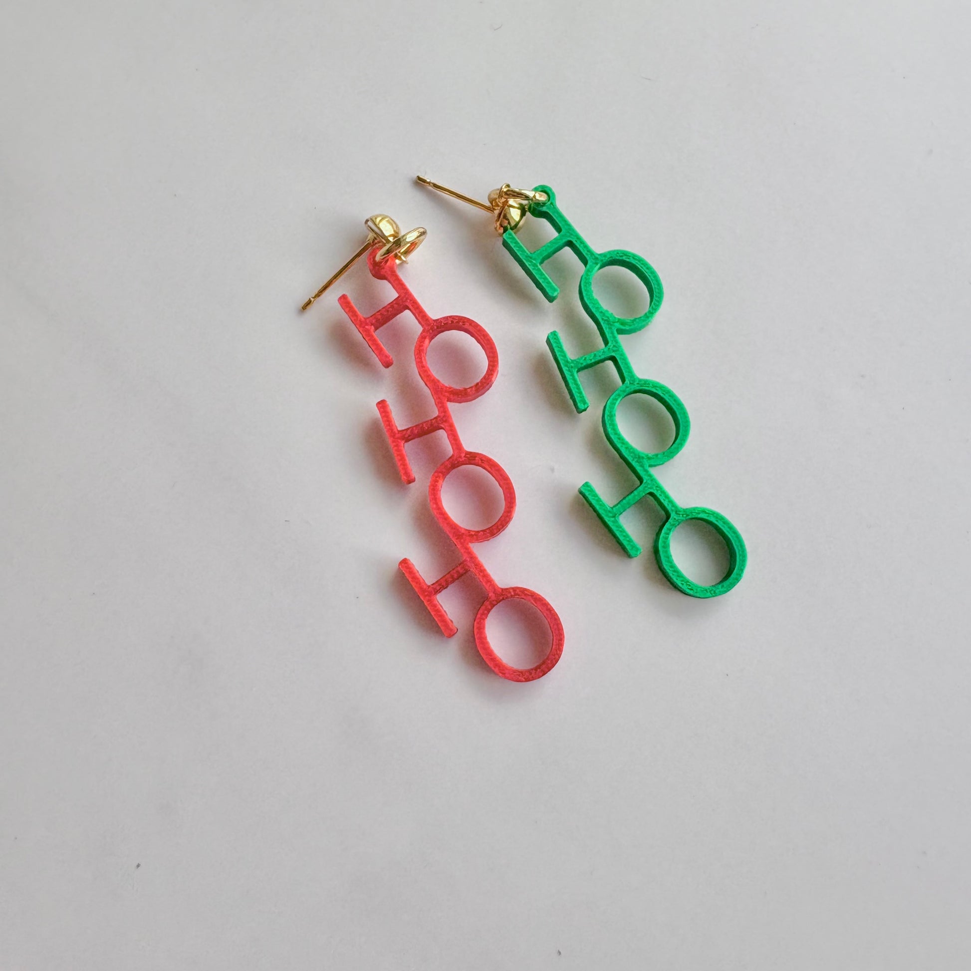 Red and green 'HO HO HO' earrings on a light gray background
