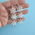 White snowflake earrings held in a hand against a light blue background