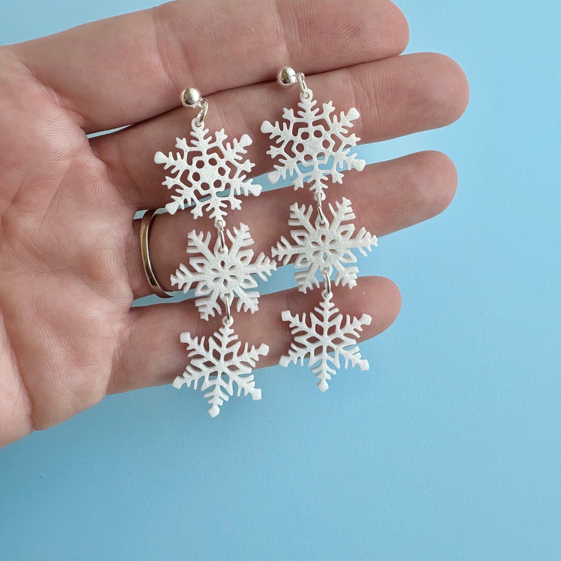White snowflake earrings held in a hand against a light blue background