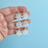 Snowflake earrings held in a hand against a light blue background