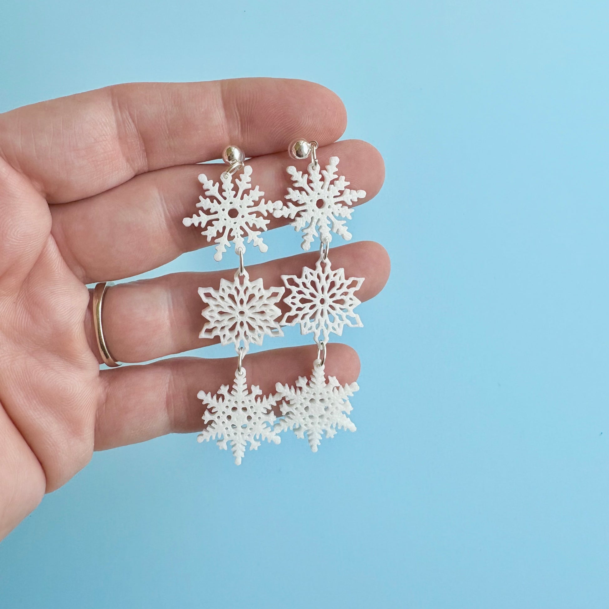 Snowflake earrings held in a hand against a light blue background