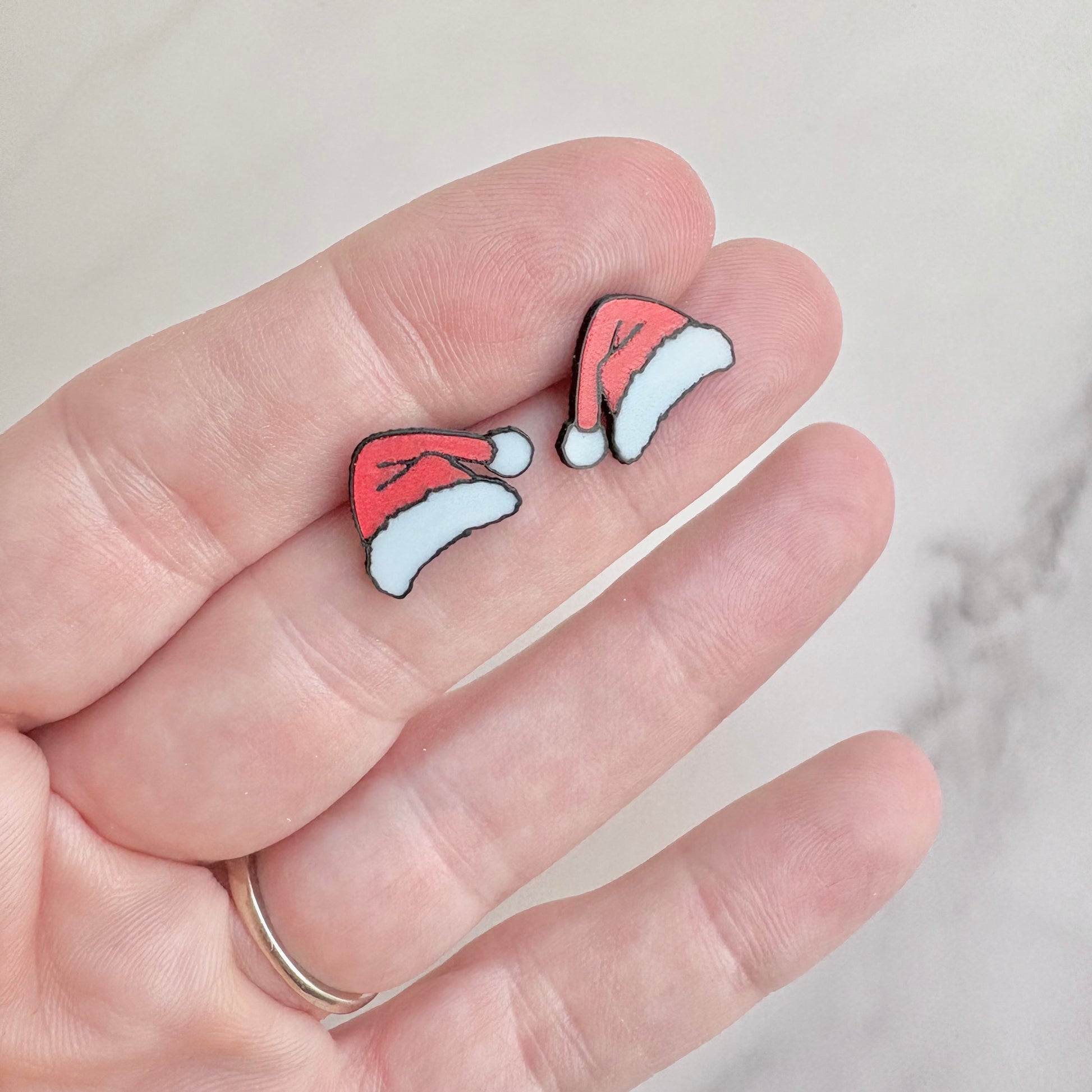 Santa hat earrings held between fingers against a neutral background