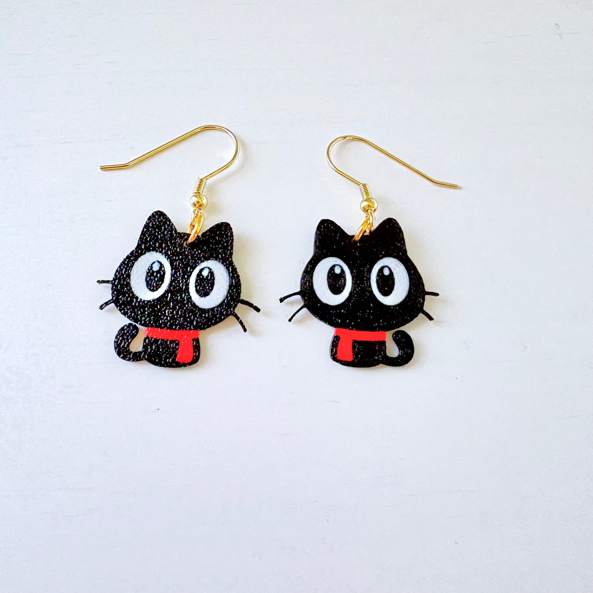 Black cat-shaped earrings with gold hooks on a white background