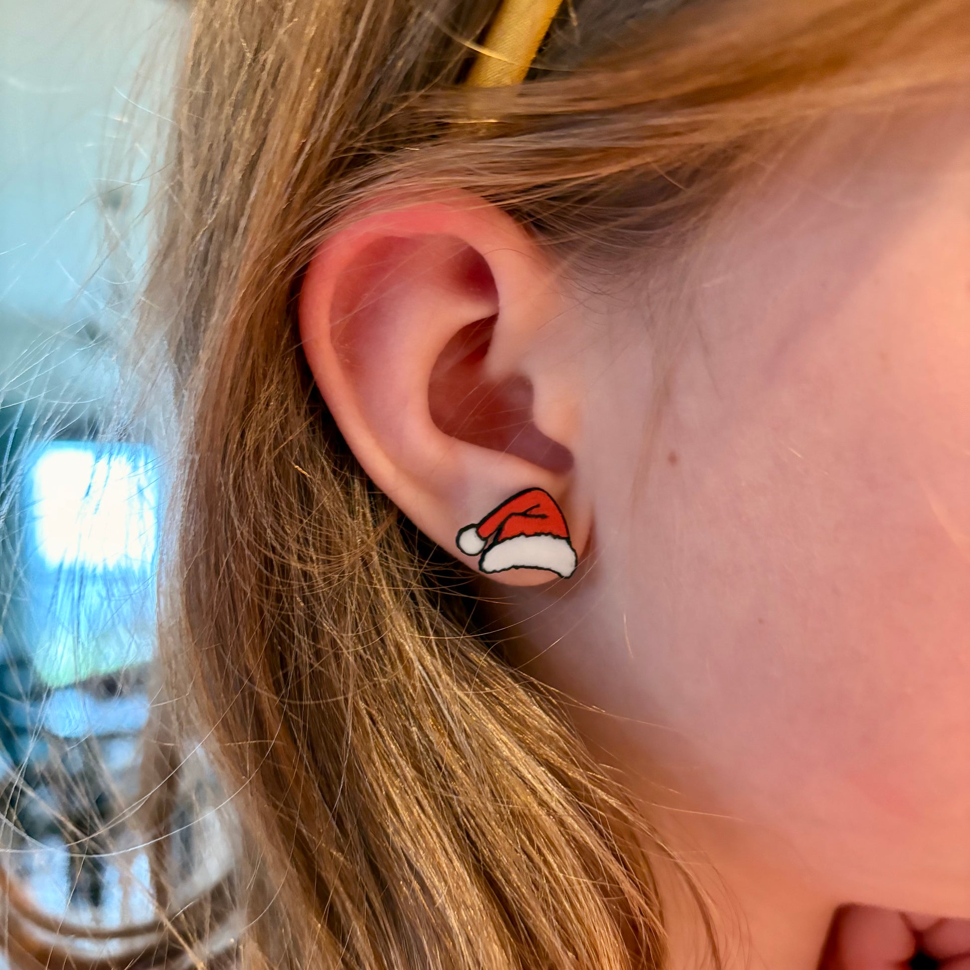 Close-up of an ear wearing a small red and white Santa hat earring.