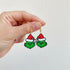 Hand holding a pair of Grinch earrings with Santa hats against a light background