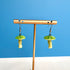 Green mushroom-shaped earrings on a gold stand against a blue background