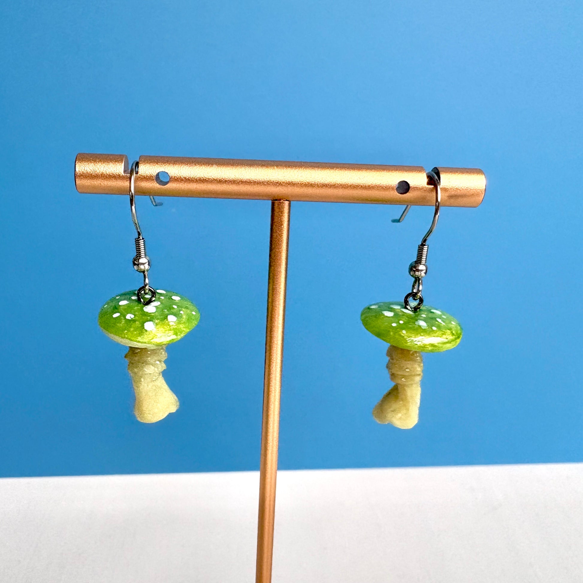Mushroom-shaped earrings on a gold stand against a blue background