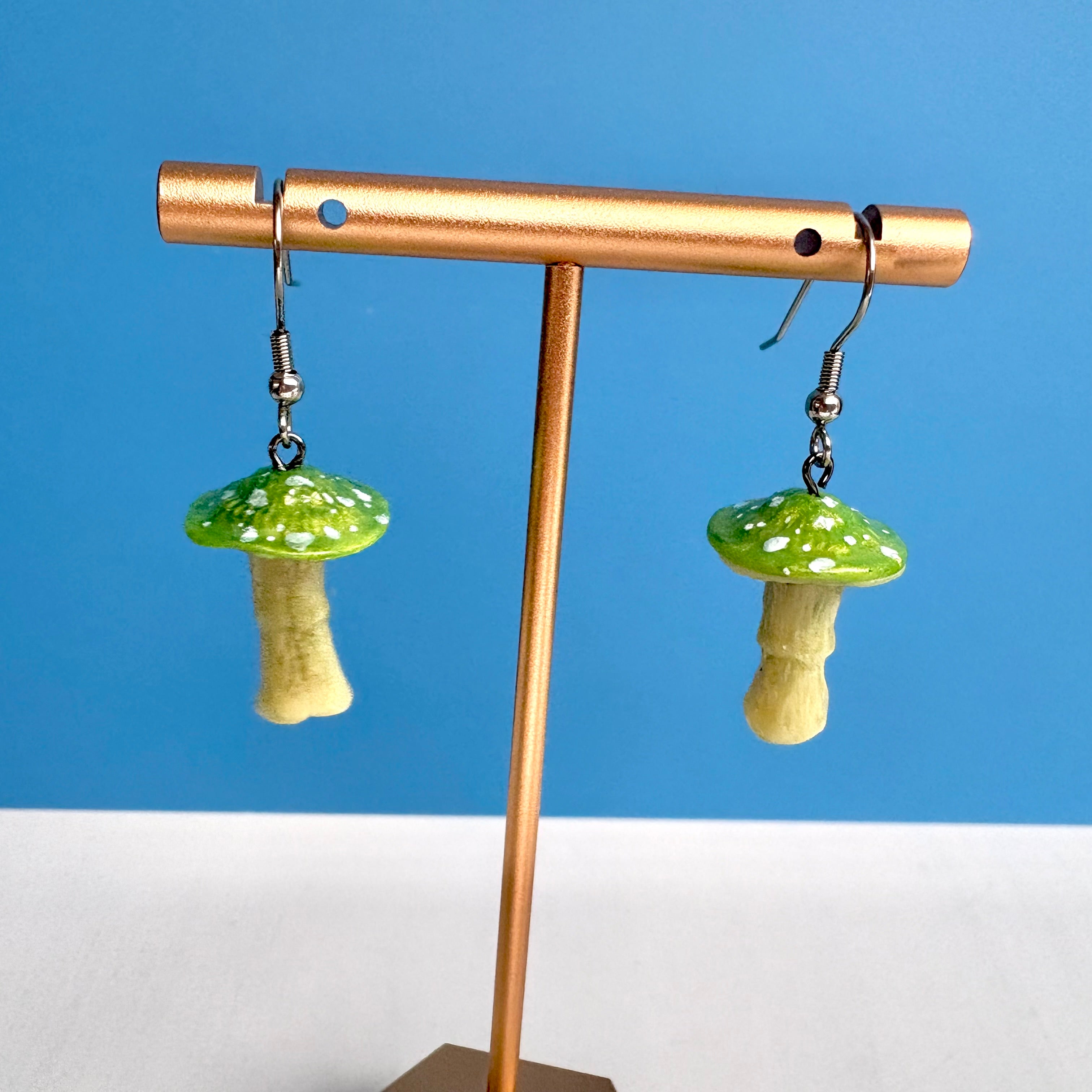 Mushroom-shaped earrings on a gold stand against a blue background