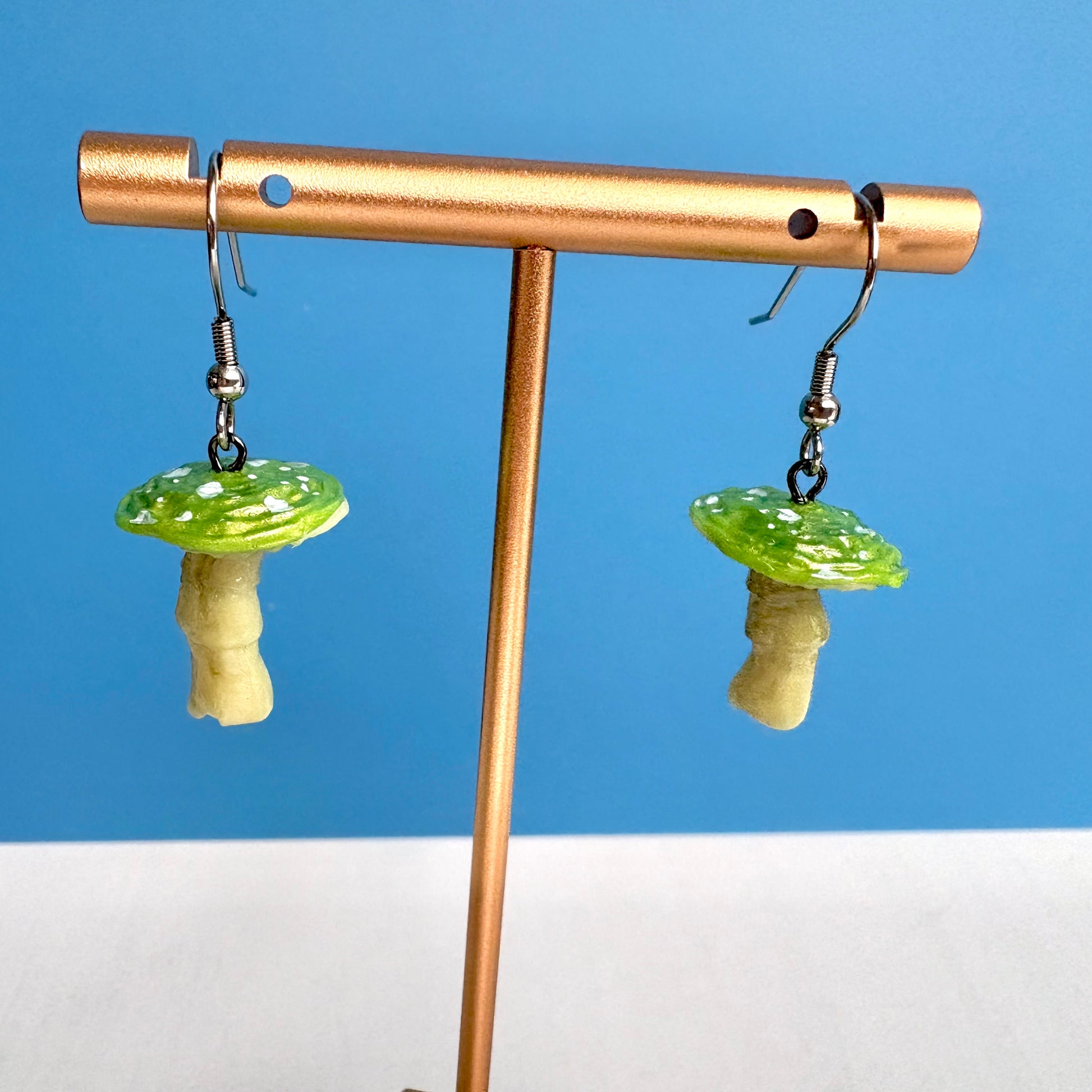 Mushroom-shaped earrings on a gold stand against a blue background