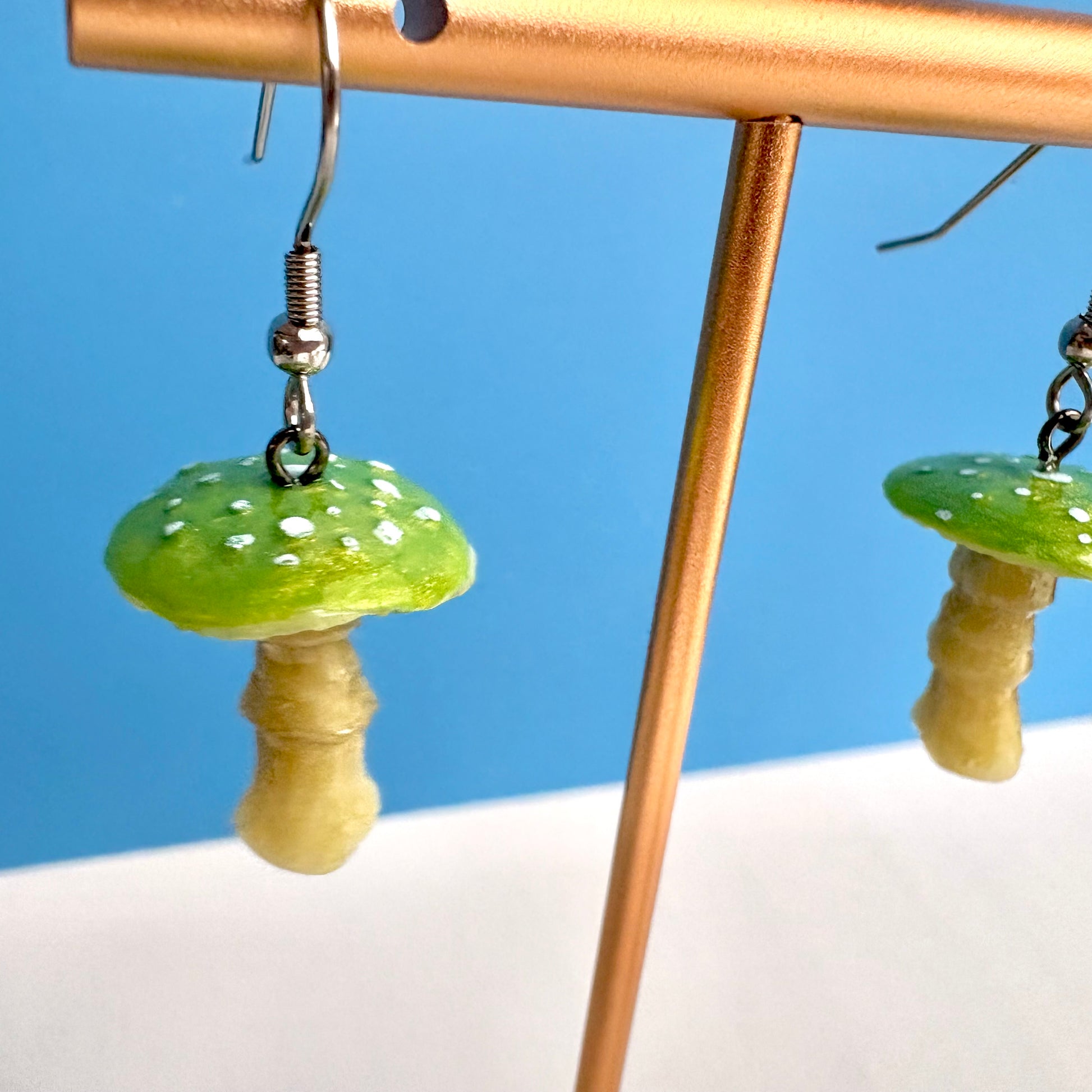 Mushroom-shaped earrings on a stand with a blue background