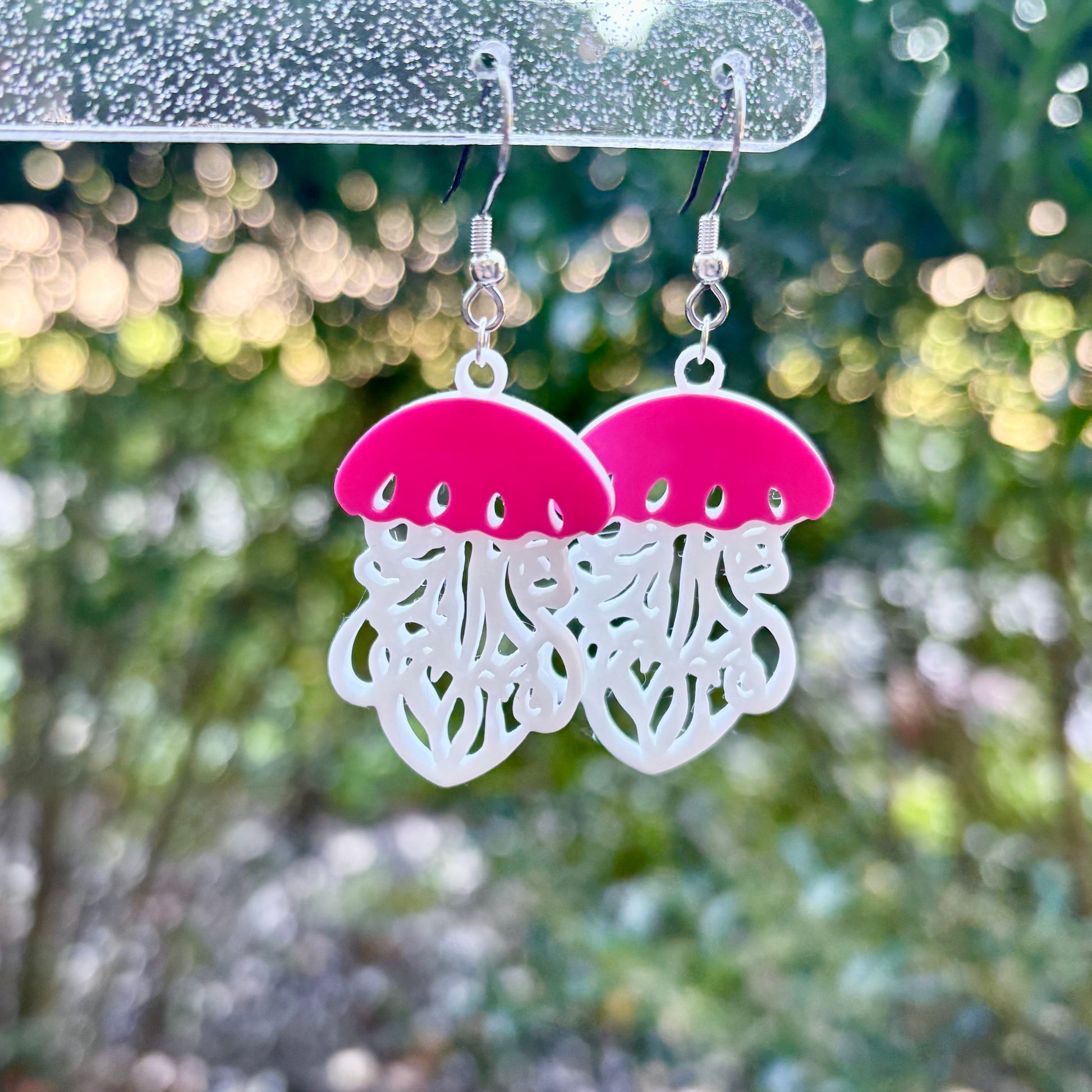 Jellyfish-shaped earrings with pink tops and white bottoms on a blurred natural background