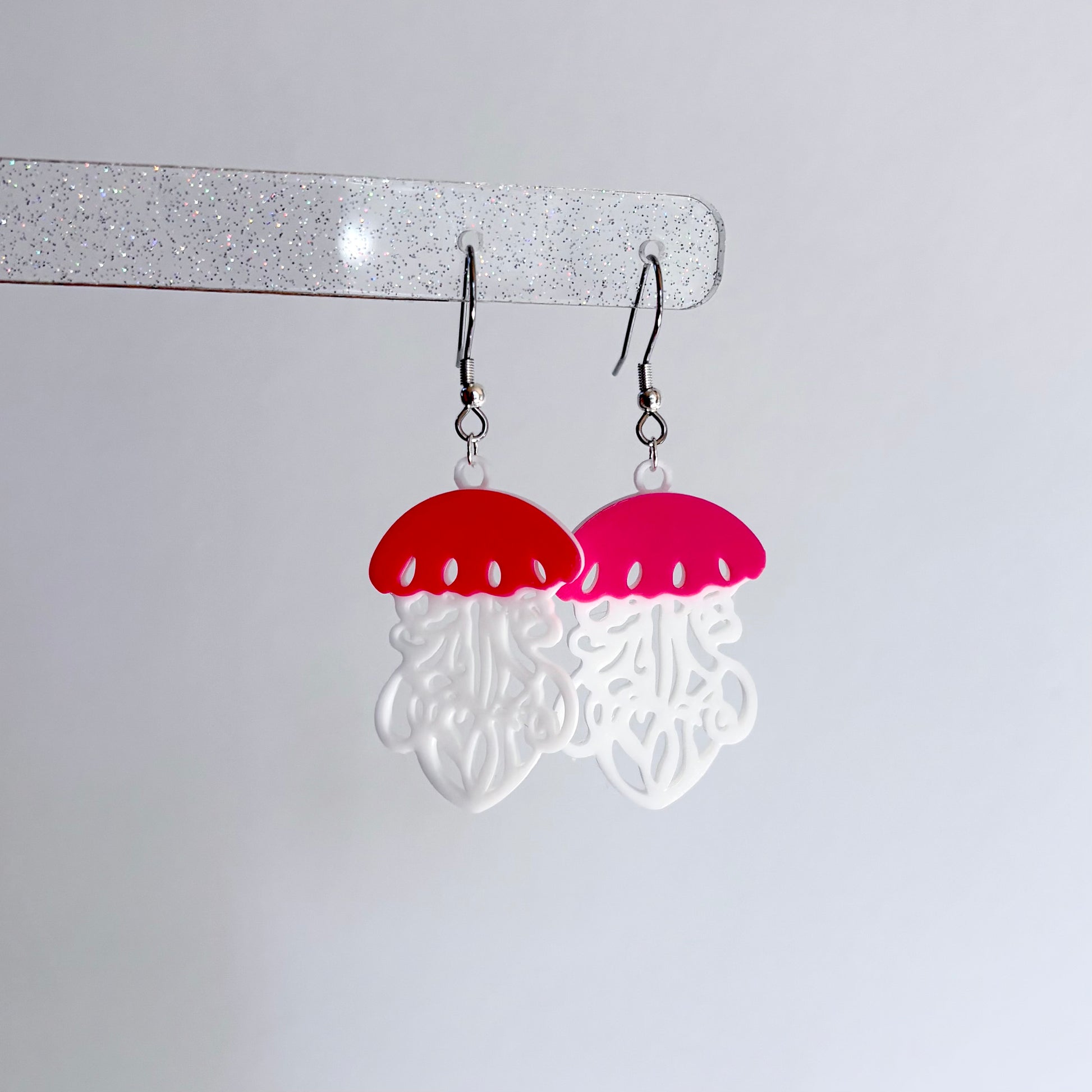 Jellyfish-shaped earrings with red tops and pink undersides on a white background