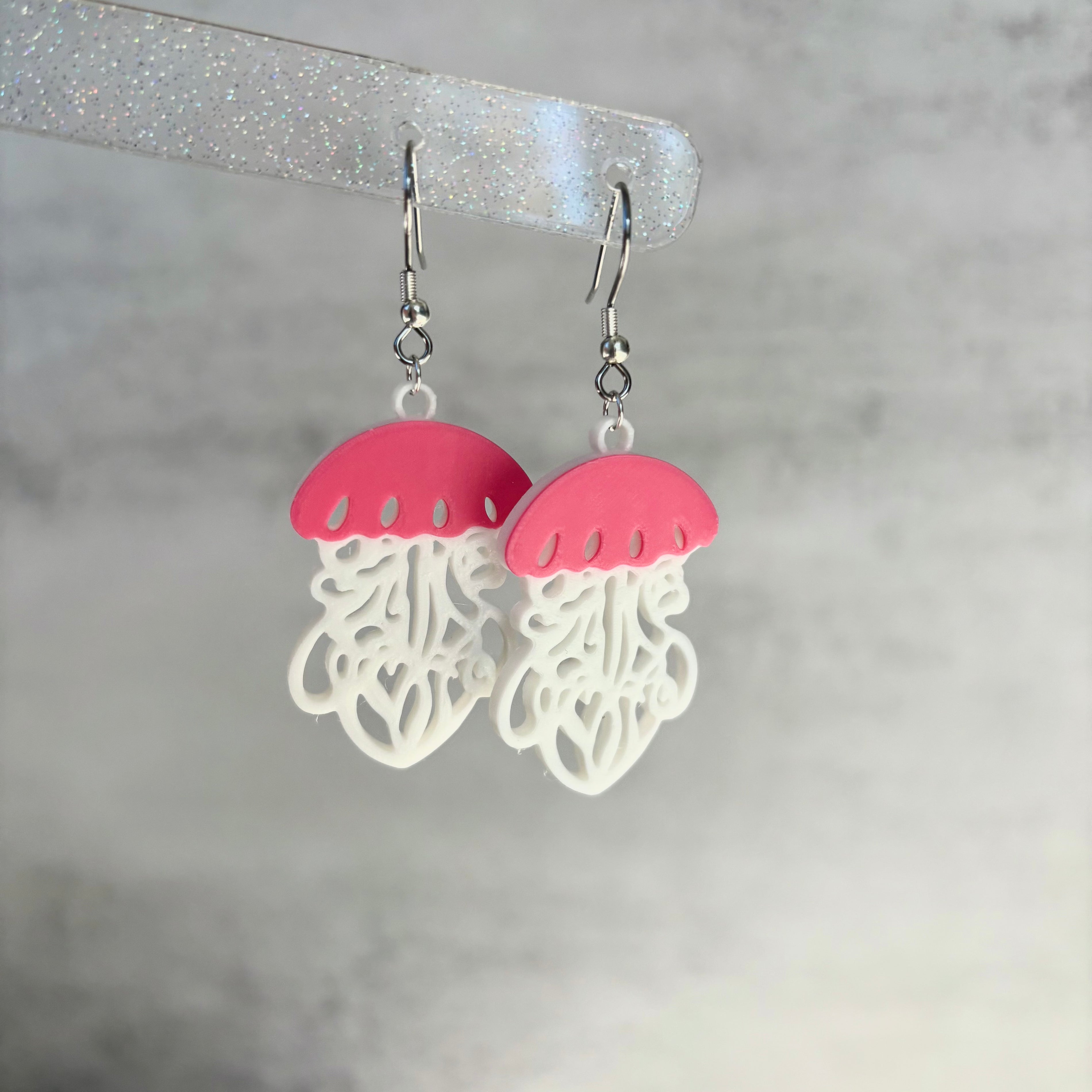 Jellyfish-shaped earrings with pink tops and white bodies on a gray background
