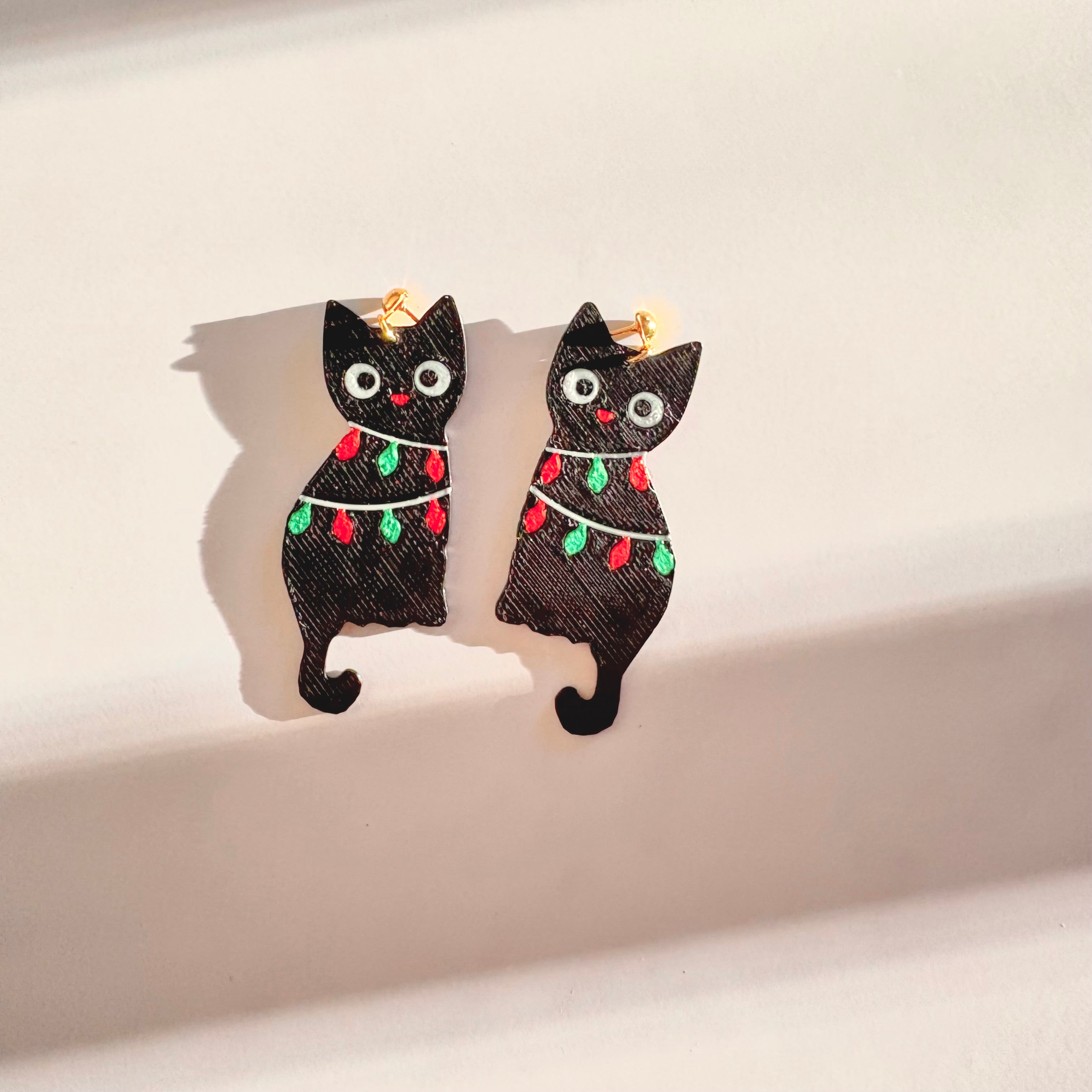 Black cat earrings with Christmas lights on a beige background