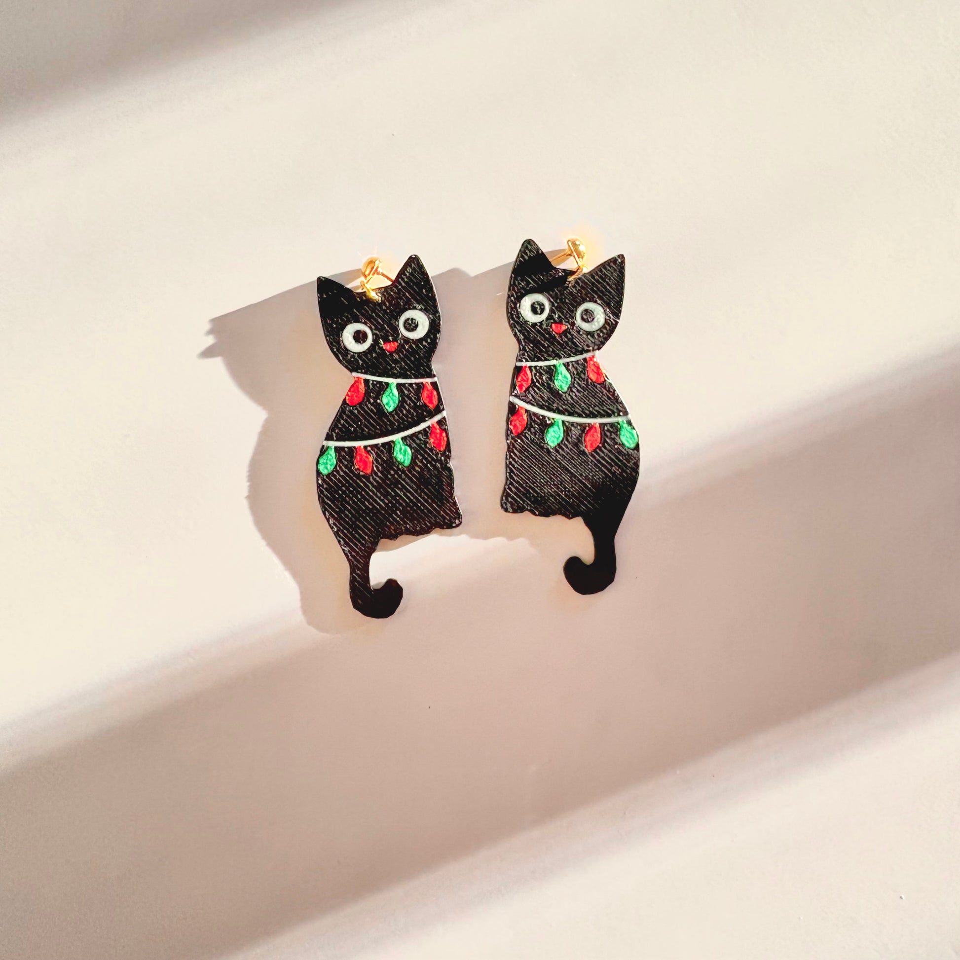 Black cat-shaped earrings with festive lights on a light background