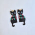 Black cat-shaped earrings with string lights on a light blue background
