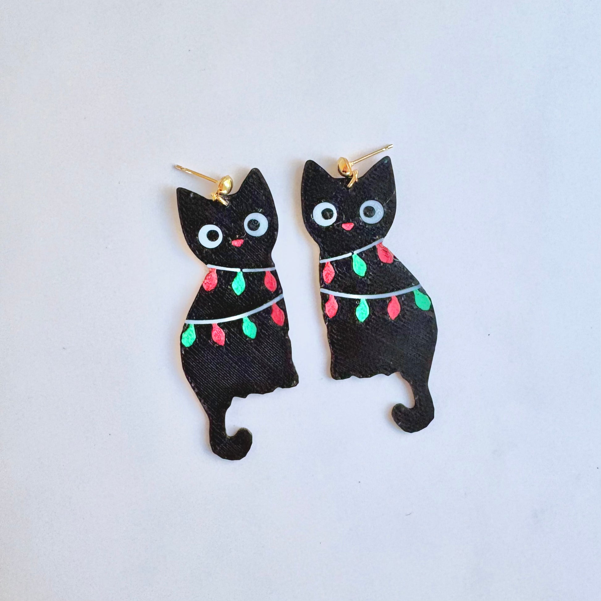 Black cat-shaped earrings with string lights on a light blue background