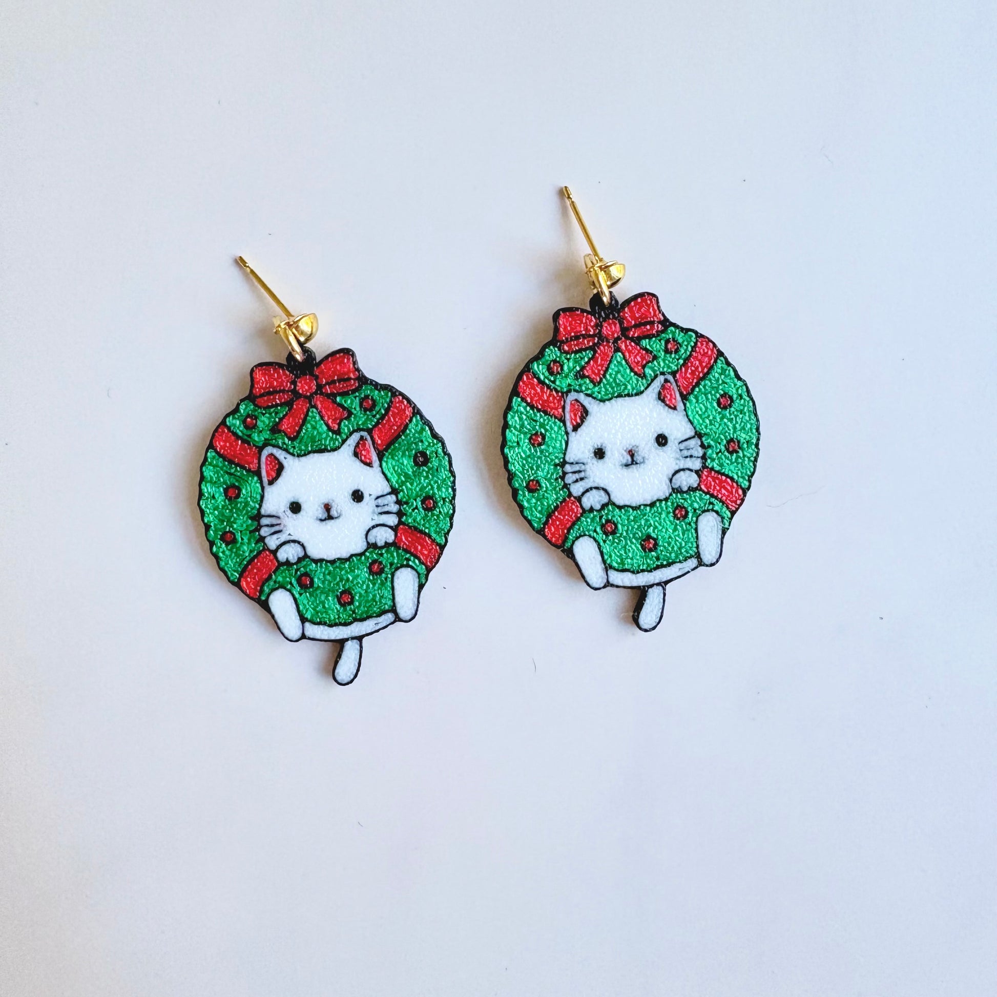 Earrings with cat design in a Christmas wreath on a light blue background