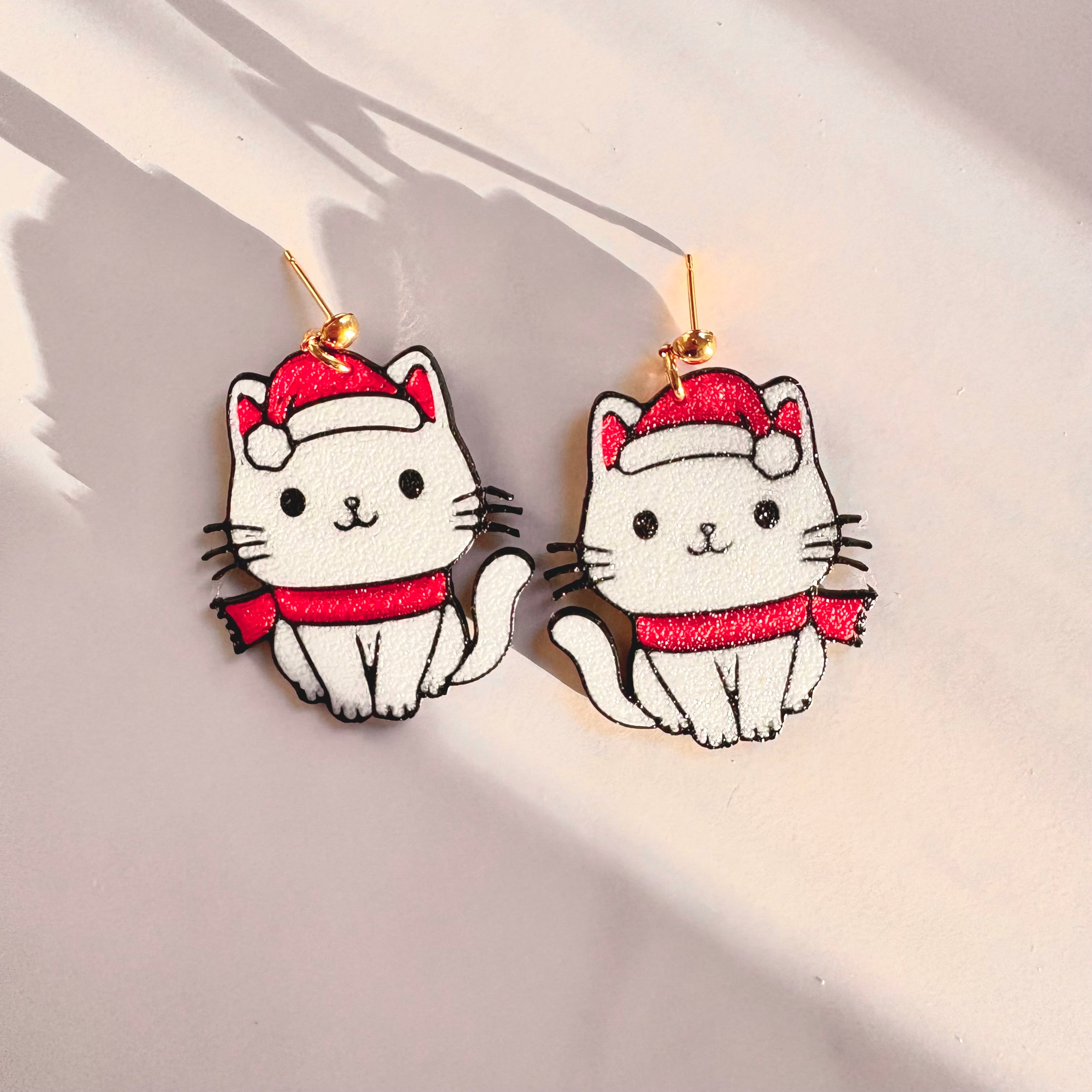 Cat-shaped earrings with red hats and scarves on a light background