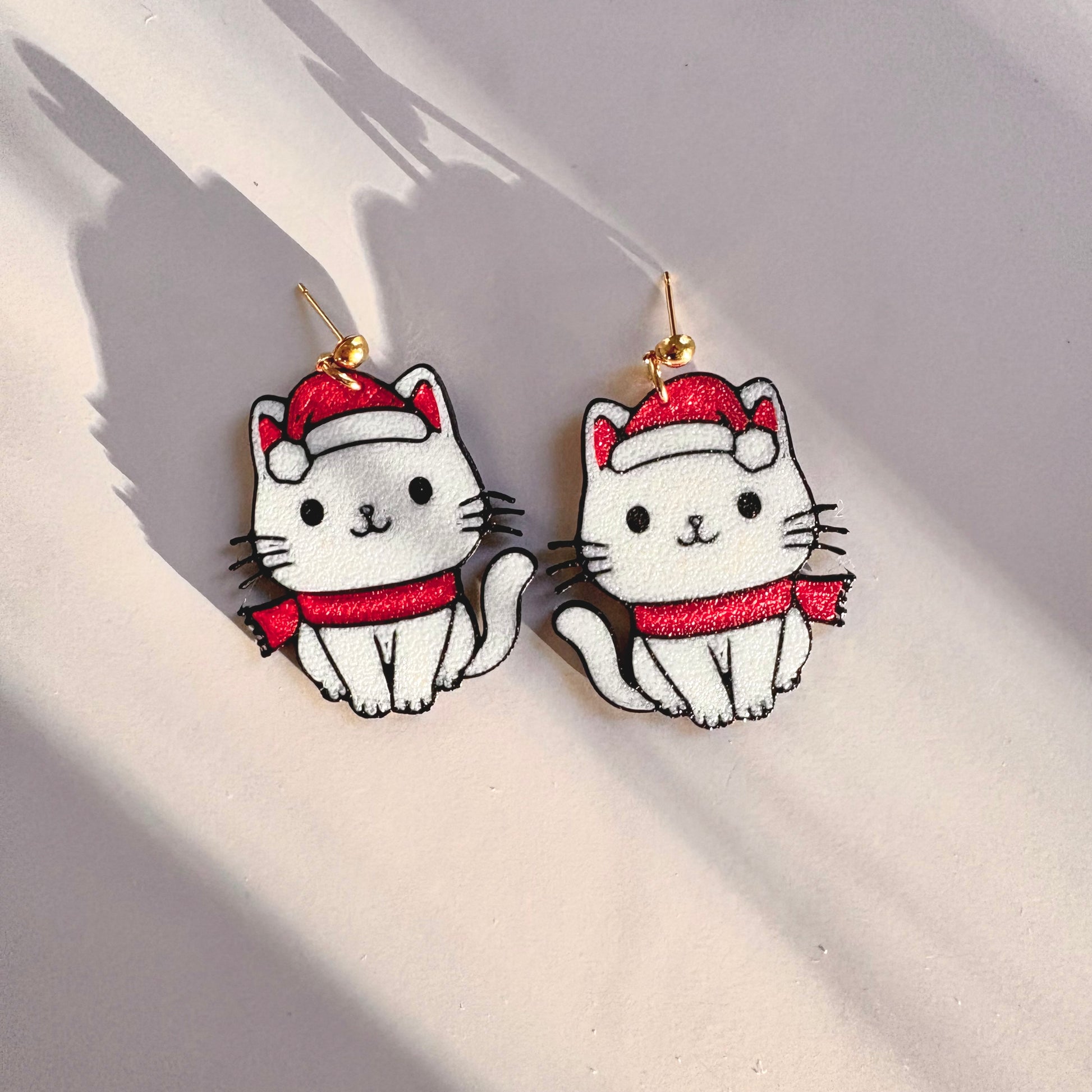 Cat-shaped earrings with red hats and scarves on a light background