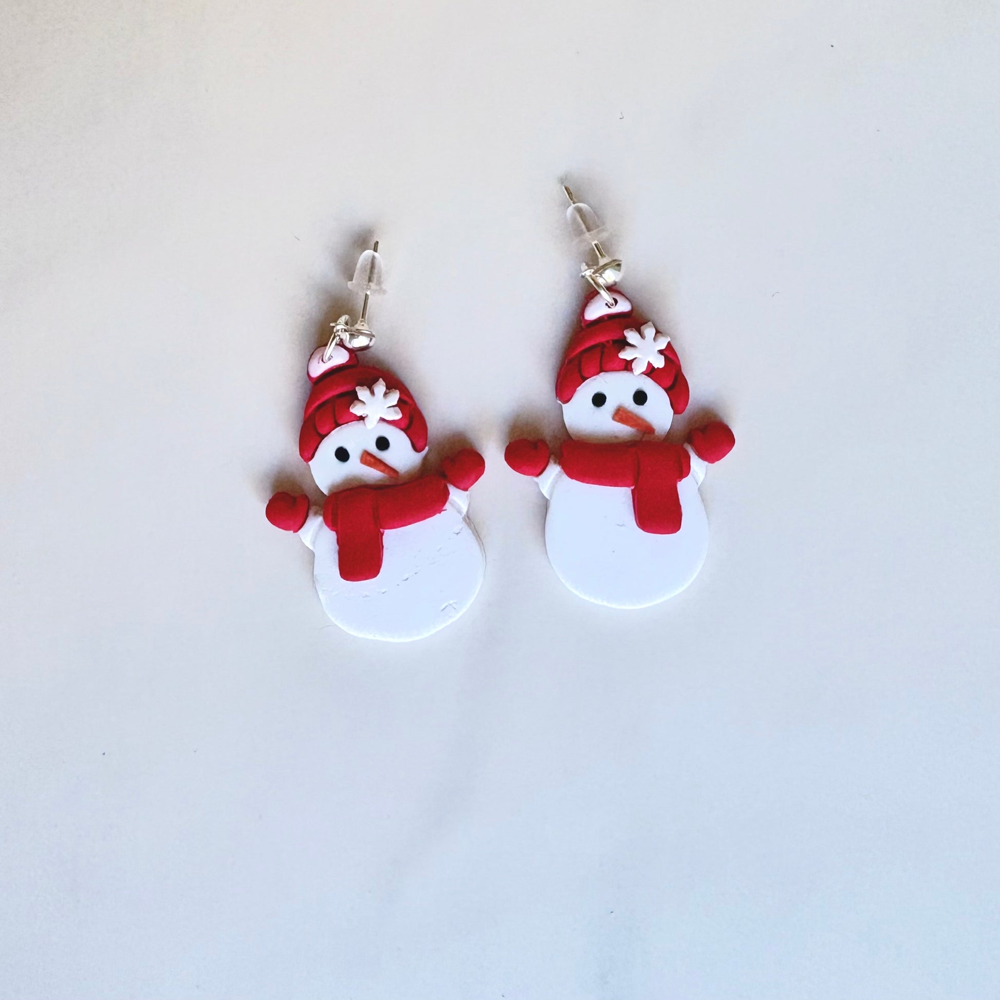 Pair of snowman-shaped earrings with red hats and scarves on a light gray background