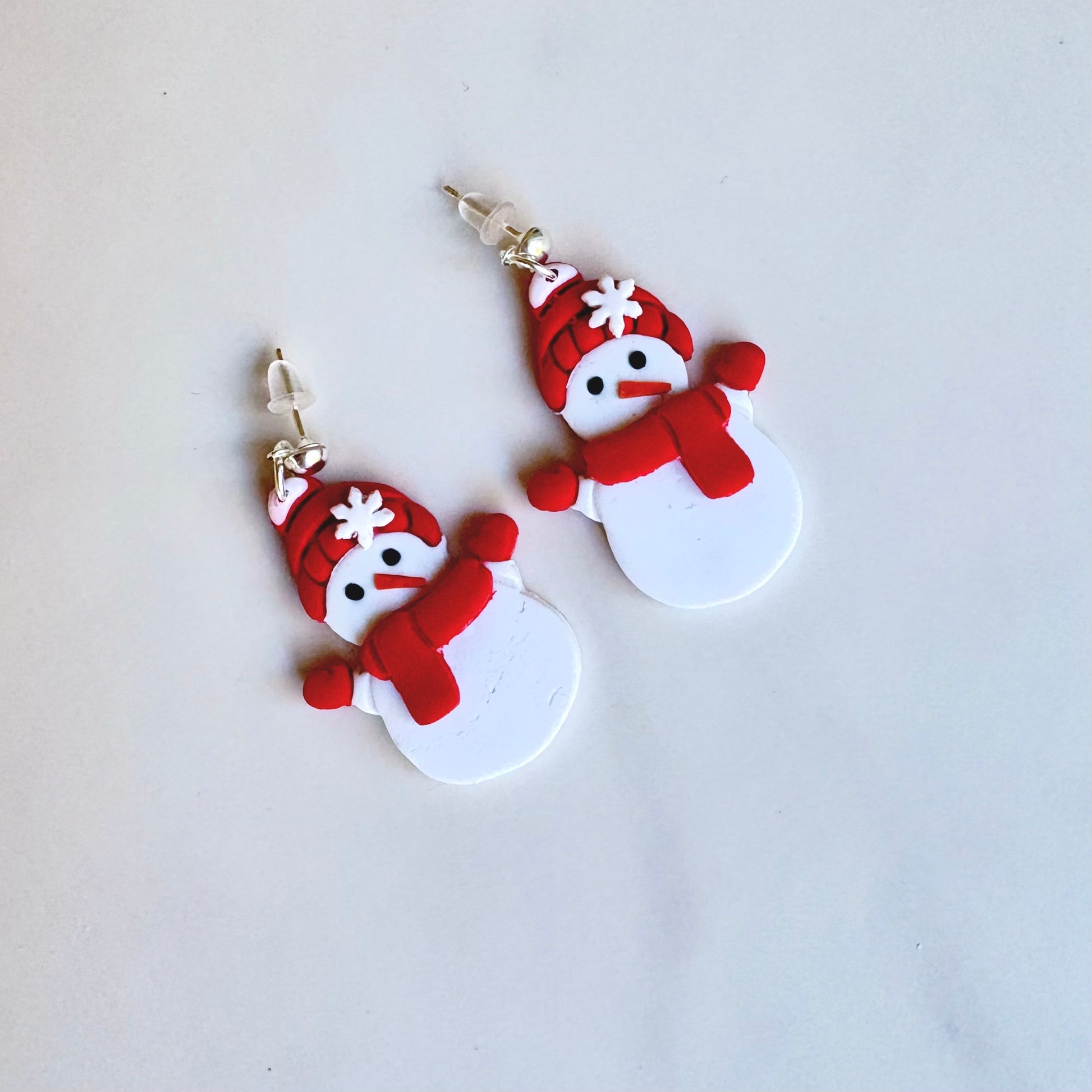 Snowman-shaped earrings with red scarves and hats on a light gray background