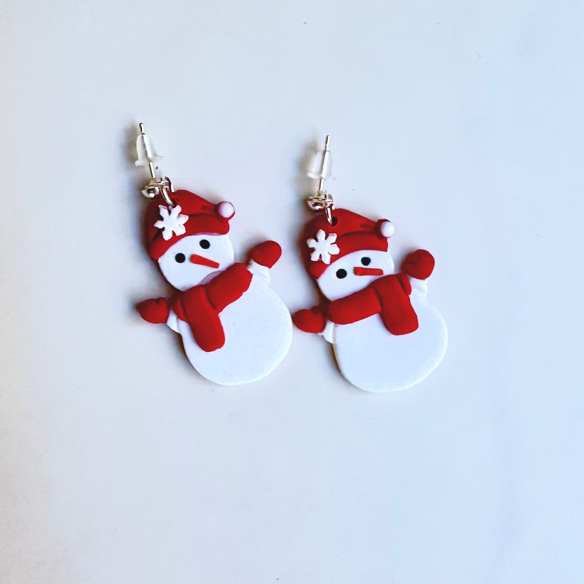 Snowman-shaped earrings with red hats and scarves on a light blue background