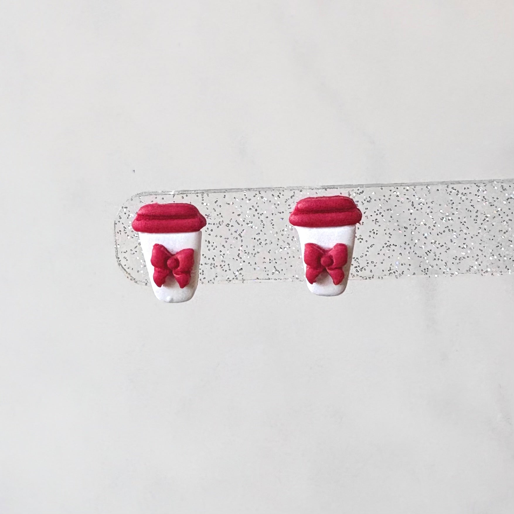 Pair of earrings shaped like red coffee cups with bows on a white background