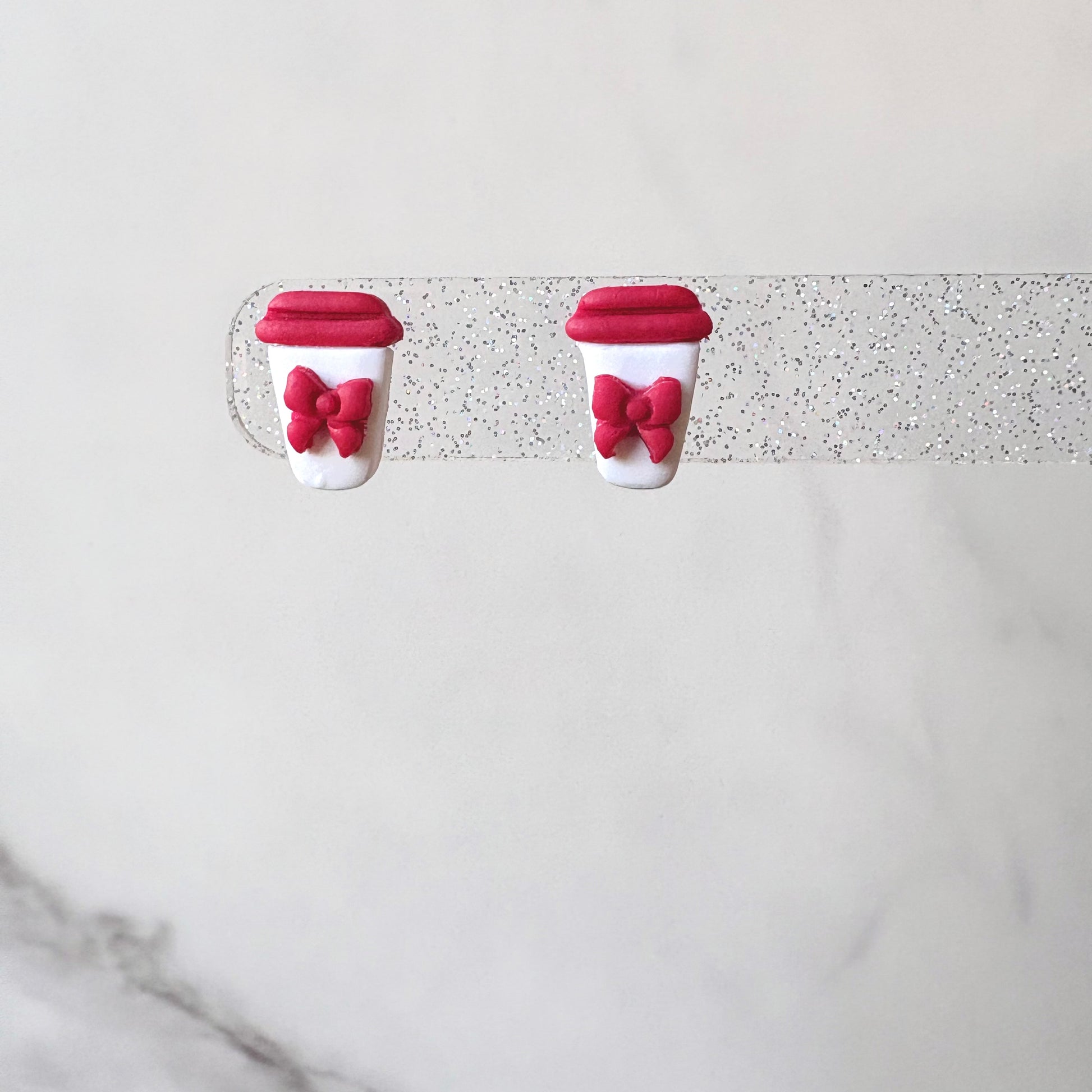 Two red and white coffee cup earrings with bows on a light gray background