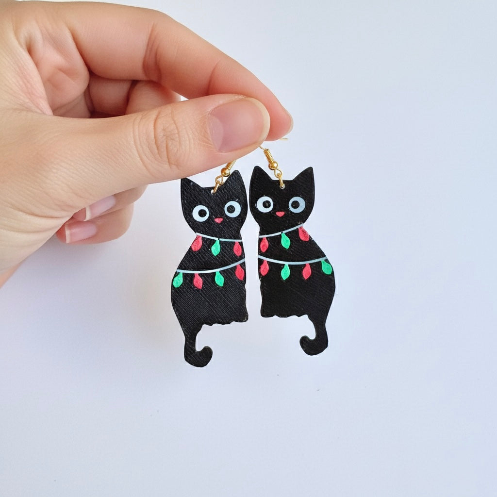 Black cat earrings with Christmas lights held by a hand on a white background