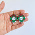 Hand holding Christmas-themed cat earrings with a white background