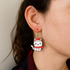 Cat-shaped earrings worn by a person with a neutral background