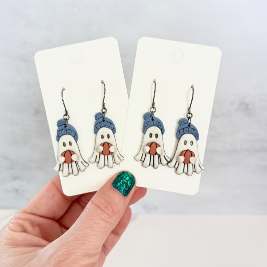 Hanging earrings featuring ghosts holding pumpkins and wearing beanie hats