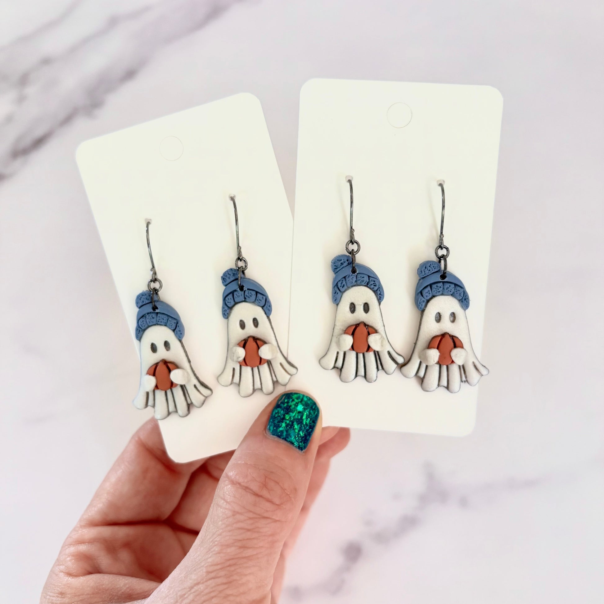 Hanging earrings featuring ghosts holding pumpkins and wearing beanie hats