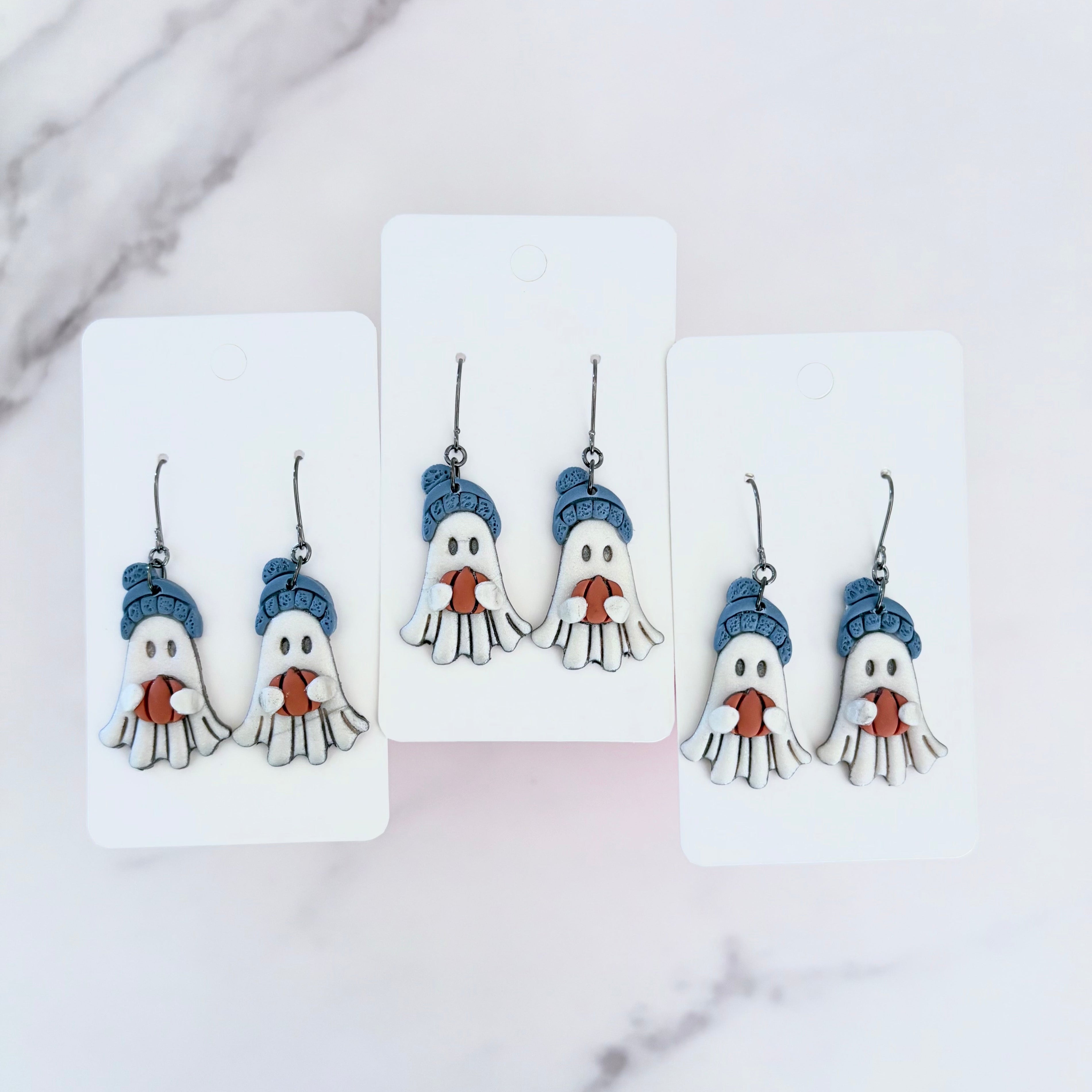 Hanging earrings featuring ghosts holding pumpkins and wearing beanie hats