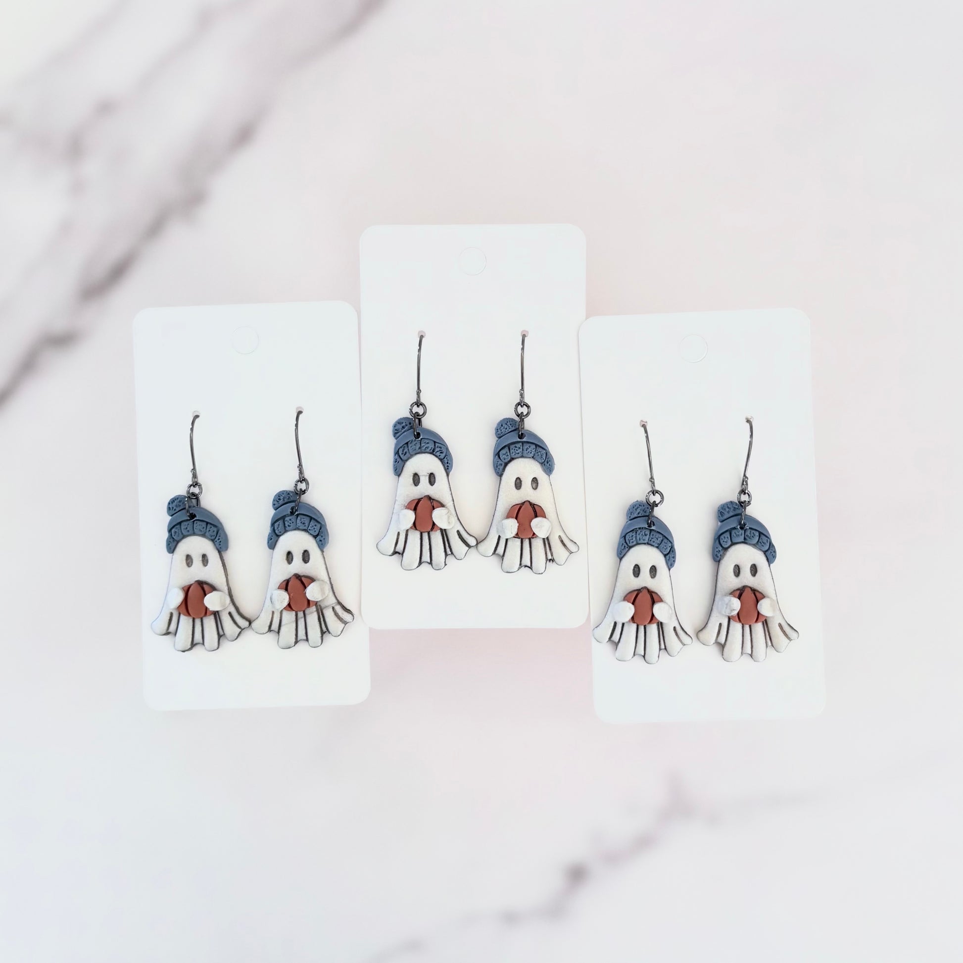 Hanging earrings featuring ghosts holding pumpkins and wearing beanie hats